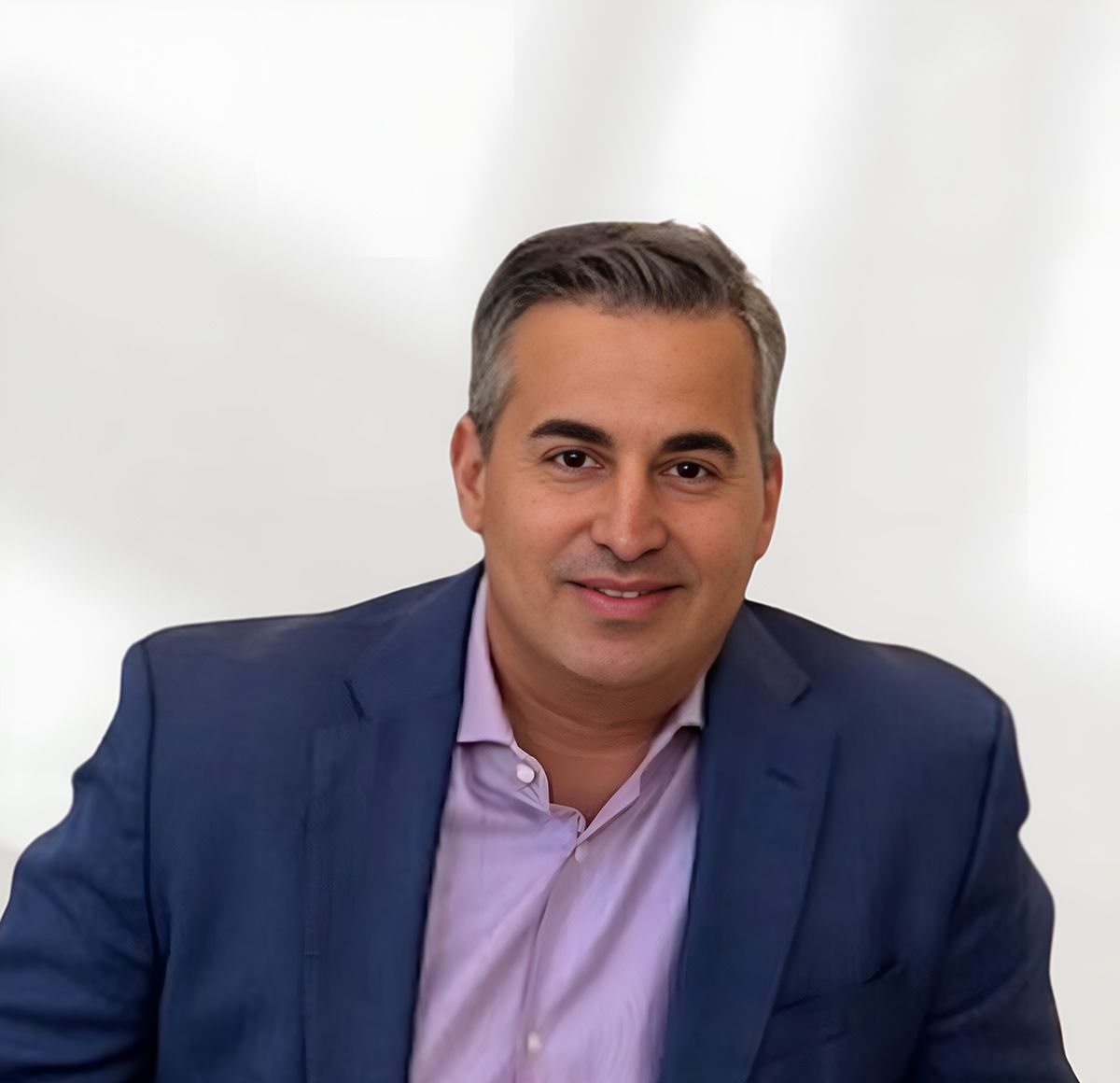 Man smiling in a suit against a light background.