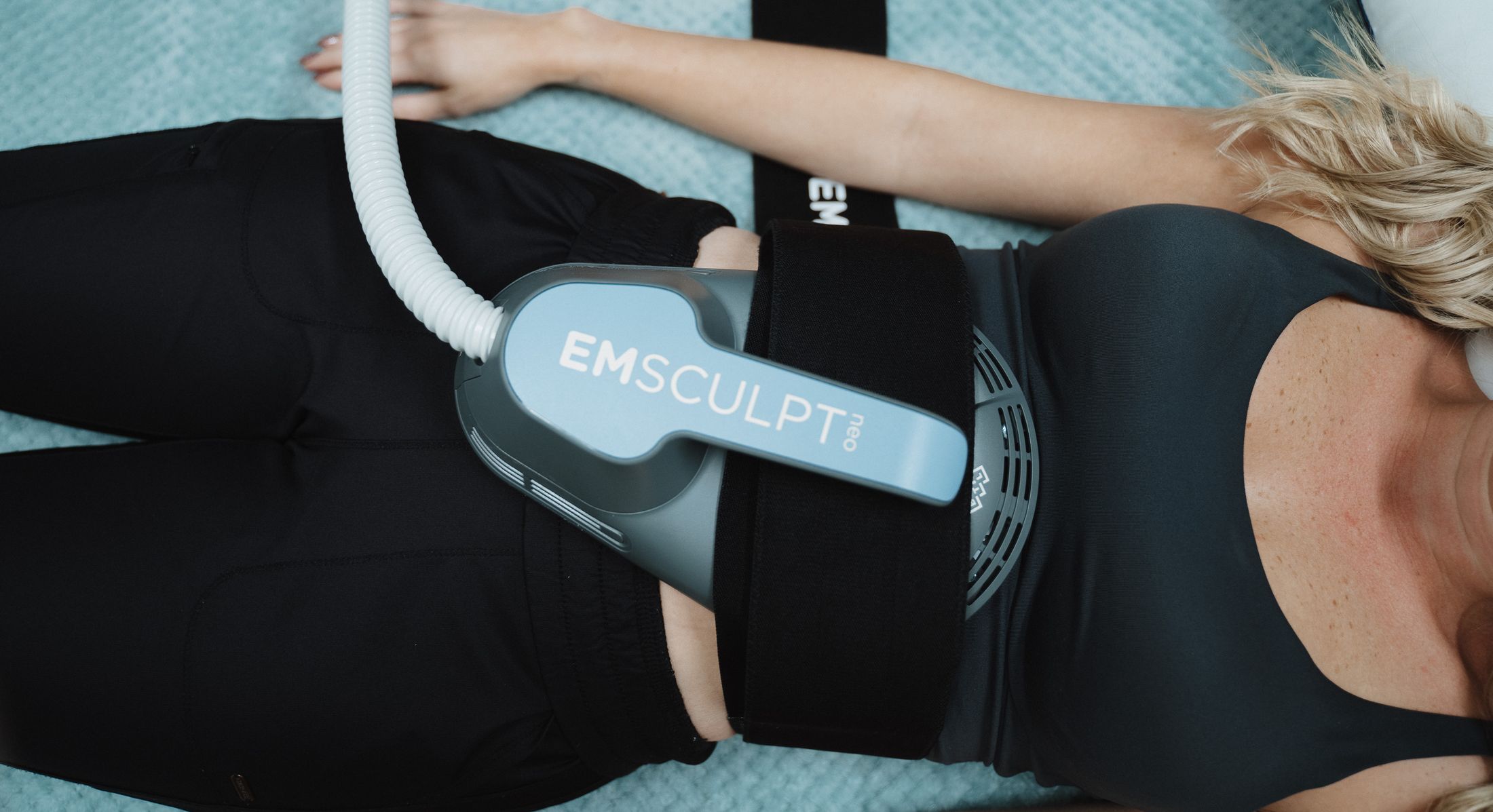 Person using EMSCULPT device for body sculpting.